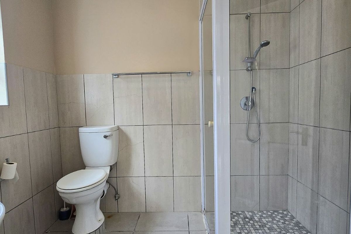 A functional bathroom featuring a glass-enclosed shower, ceramic wall tiling, a standard toilet, and a window for natural ventilation.