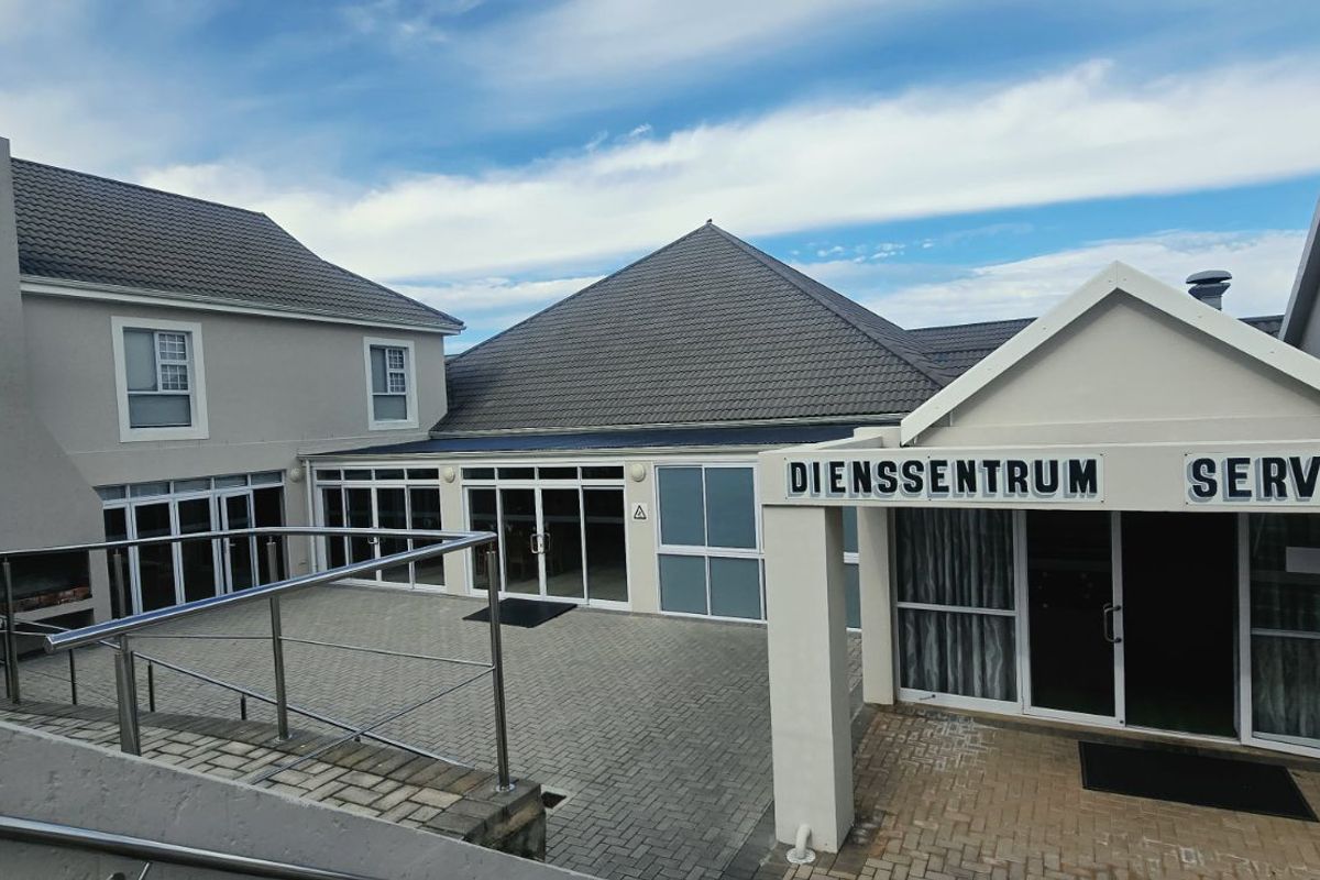 Exterior view of a paved courtyard area featuring a built-in braai, stainless steel railings, and access to a service center building.