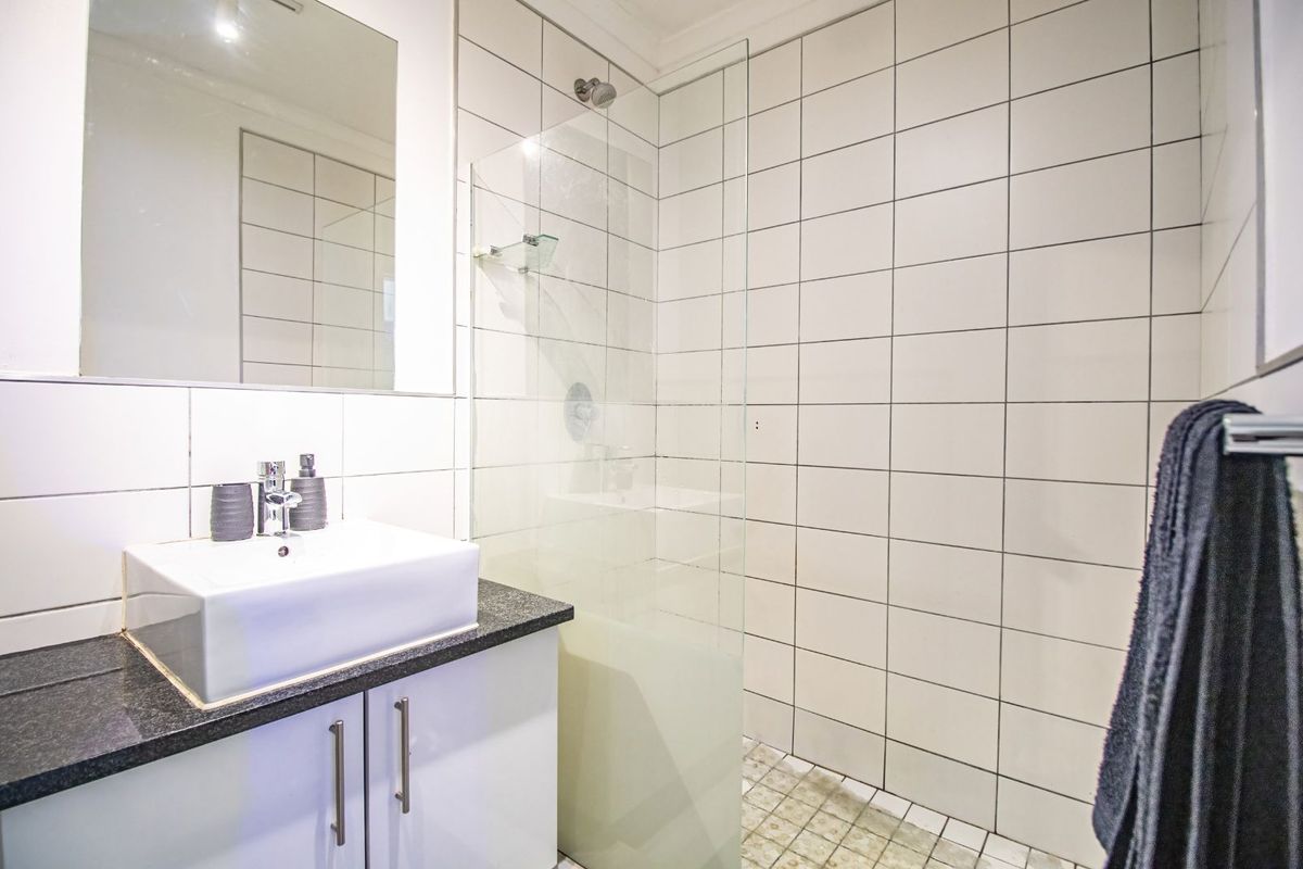Modern bathroom featuring a white vanity with a countertop basin, a frameless glass shower enclosure, and white wall tiling.