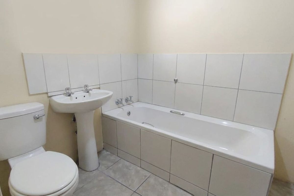 A functional bathroom featuring a white pedestal basin, a standard bathtub with tiled surround, and a matching toilet.