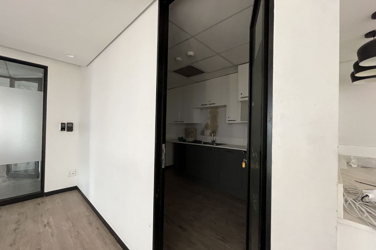 A view from an office space into a small kitchenette area featuring built-in cabinetry, a sink, and a drop ceiling.