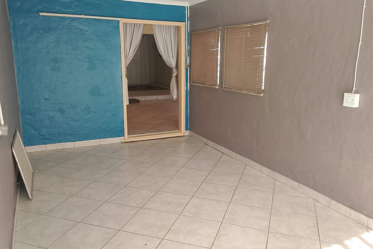 An empty living area featuring tiled flooring, a sliding door leading to an adjacent room, and dual-tone painted walls with fitted window blinds.