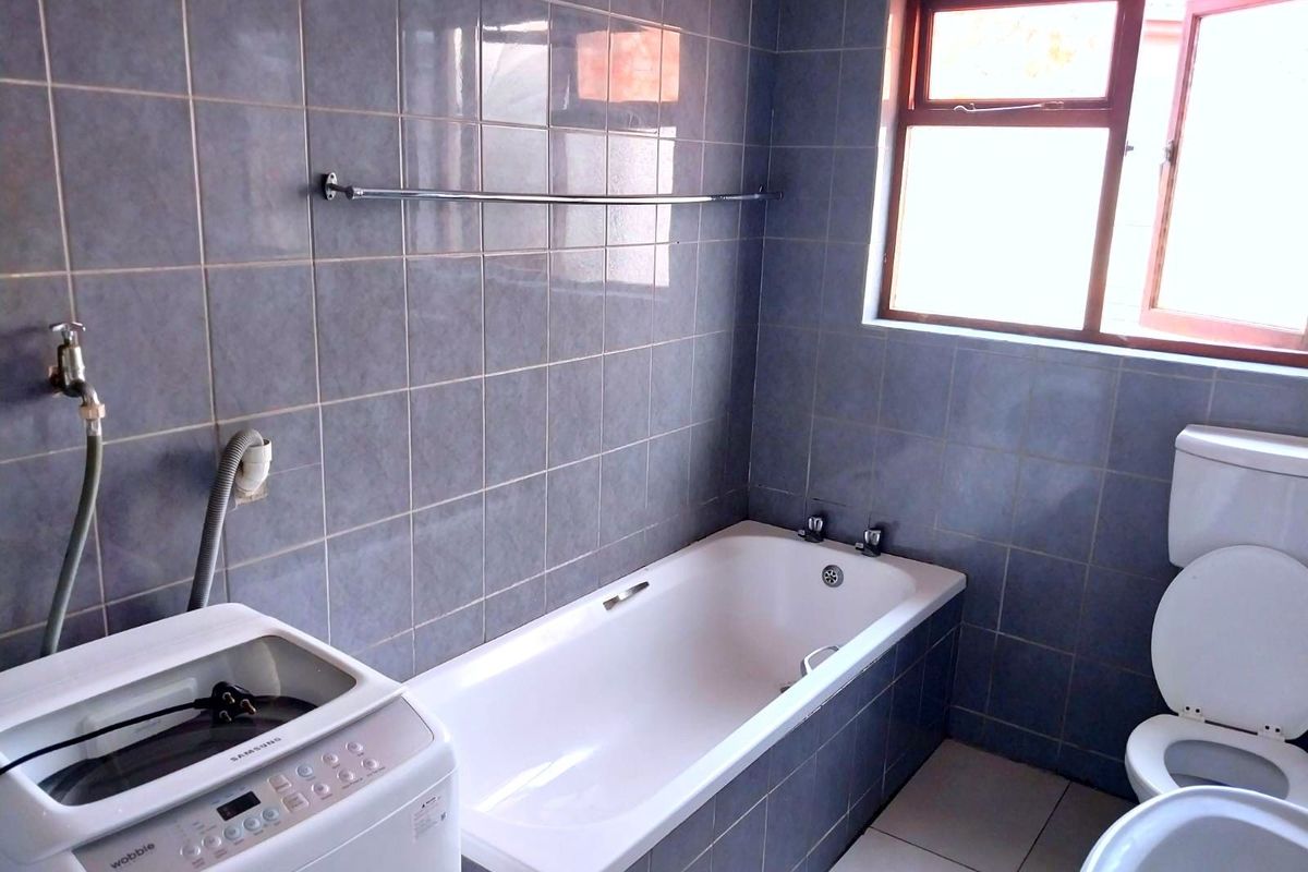 A functional bathroom featuring a built-in bathtub, toilet, and dedicated laundry plumbing connections for a washing machine.