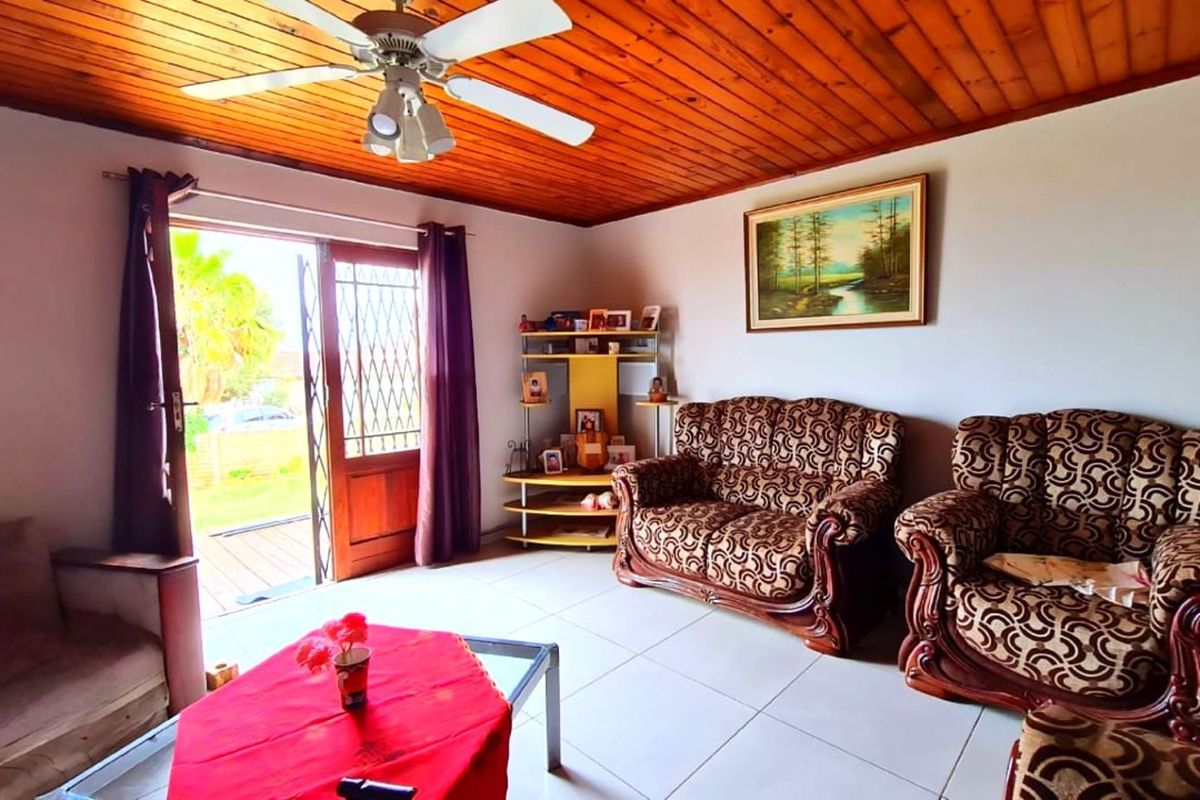 A living room featuring a timber-clad ceiling, ceiling fan, and tiled flooring, with direct access to an outdoor area through a security gate.