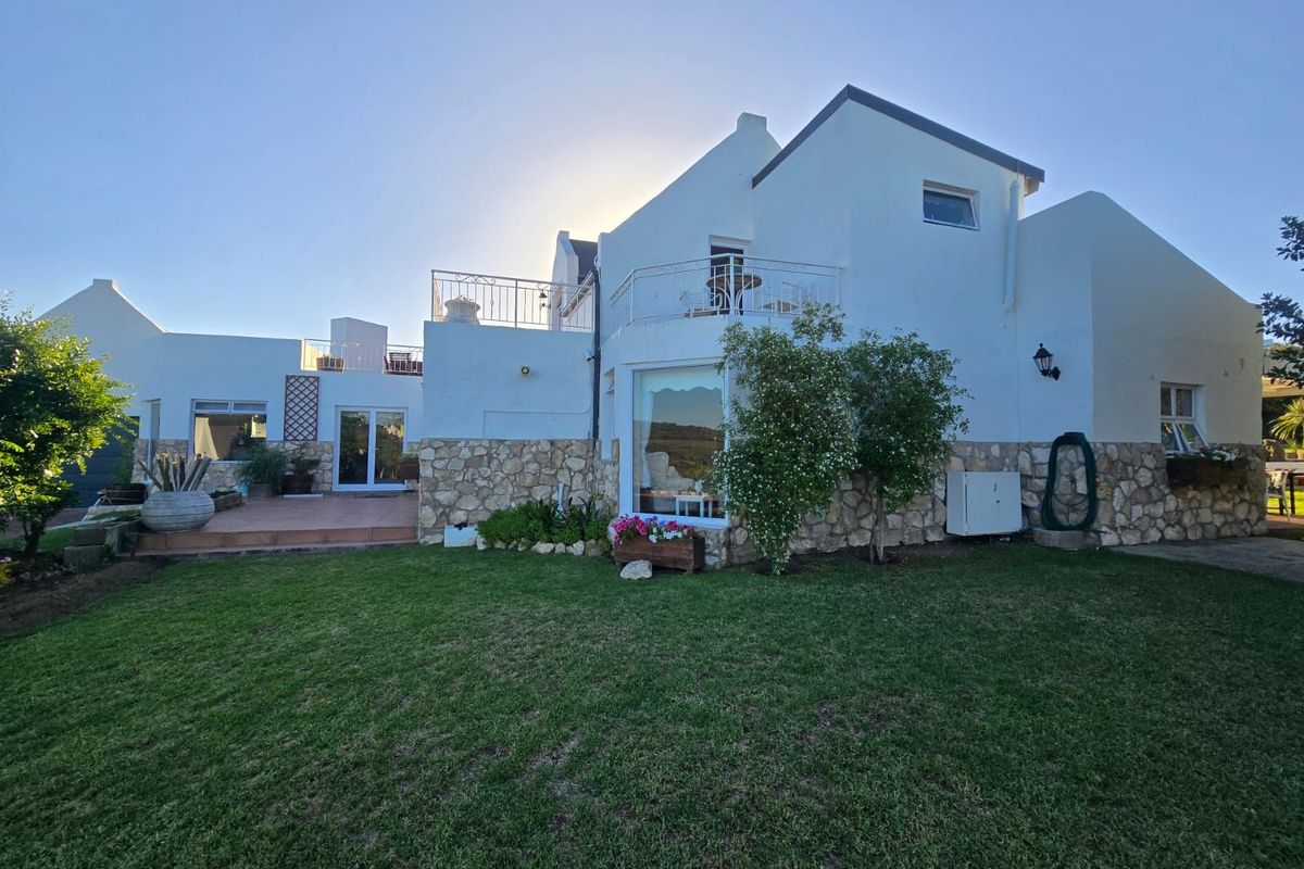 Rear view of the property featuring a white facade with stone cladding, a lawned garden, and an elevated balcony area.
