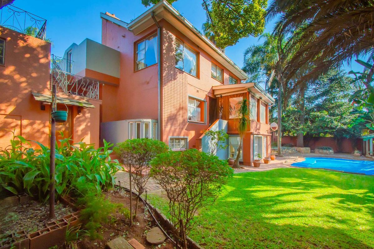 Rear view of a multi-story residential property featuring a swimming pool, landscaped garden, and paved patio area.