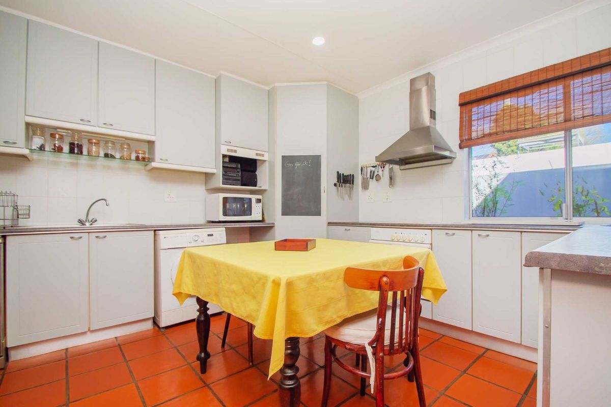 A functional kitchen featuring light-toned cabinetry, a stainless steel extractor fan, tiled flooring, and a built-in sink area with integrated appliance space.