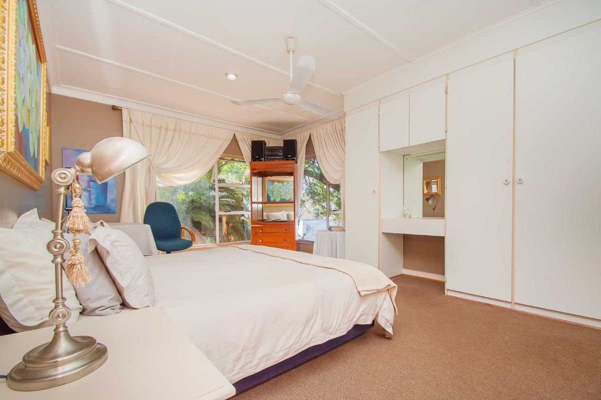 A spacious bedroom featuring built-in floor-to-ceiling wardrobes with an integrated vanity area, carpeted flooring, and a ceiling fan.