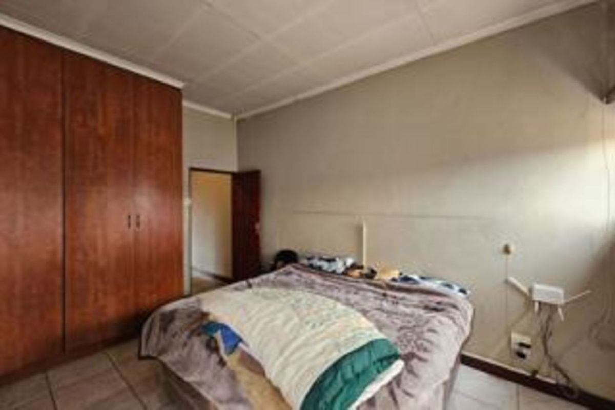 A bedroom featuring built-in wooden cupboards and tiled flooring, offering a functional space with potential for cosmetic updates.