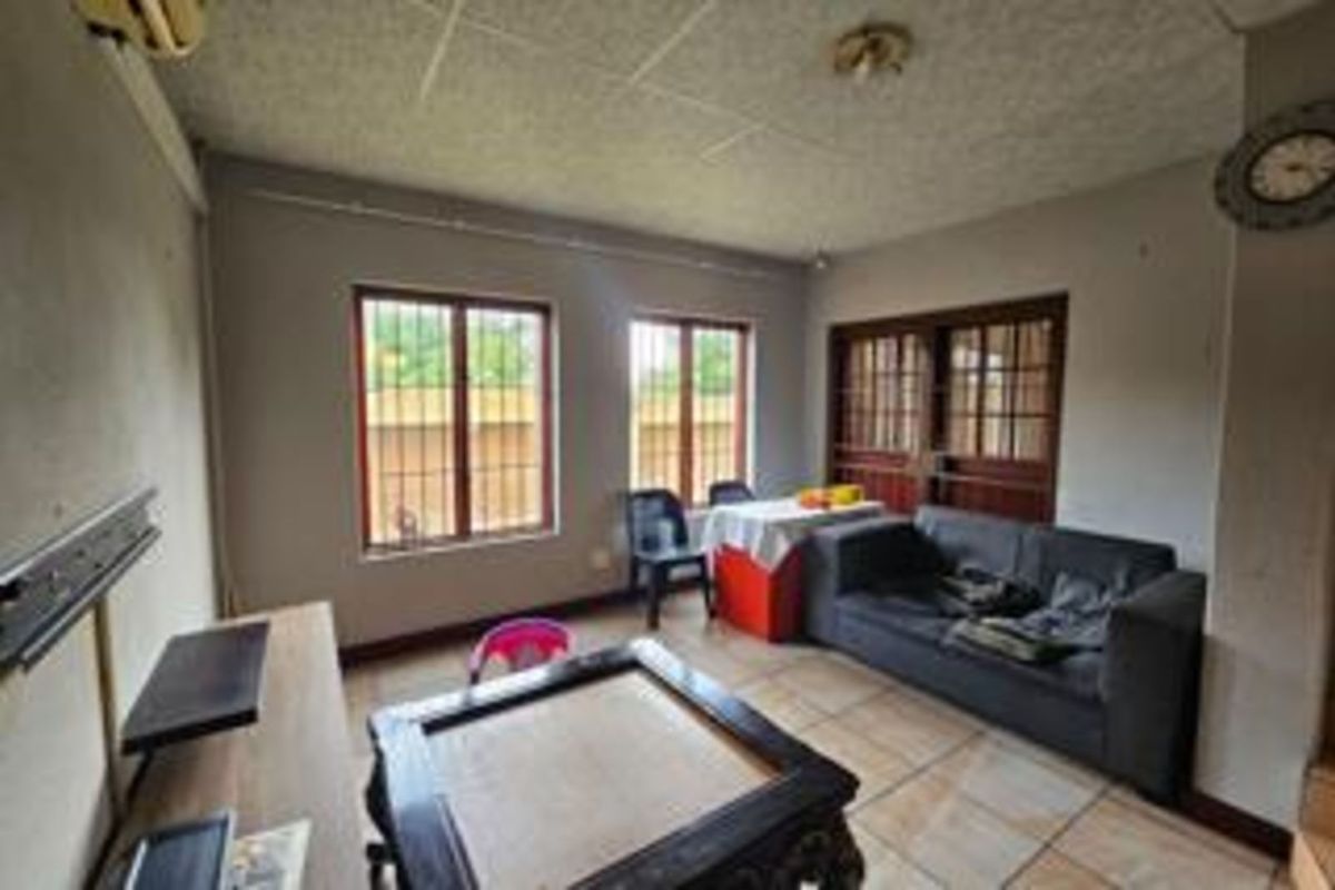 A living area featuring tiled flooring, security bars on windows, and a wooden door frame, providing a functional space for relaxation.
