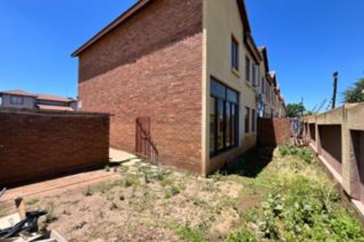 Rear view of the townhouse featuring exposed brick facade, large windows, and an expansive, unlandscaped garden area enclosed by perimeter walls.