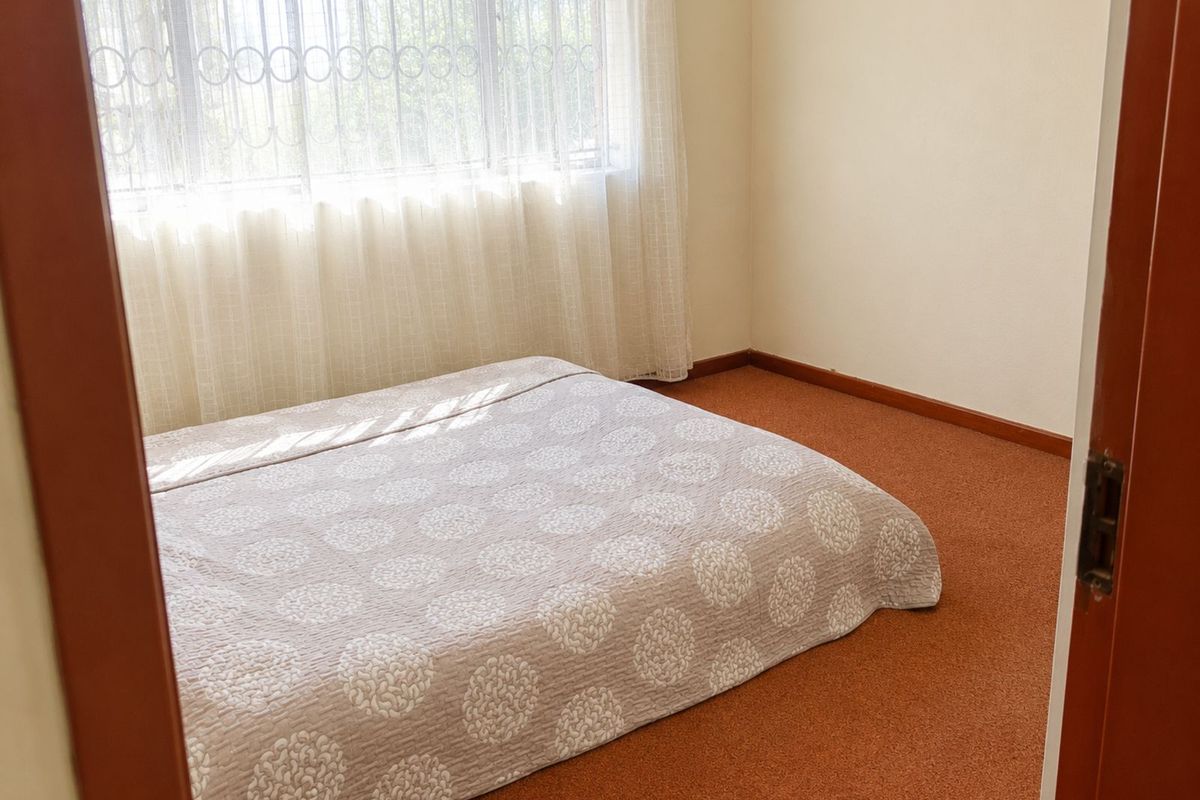 A bedroom featuring carpeted flooring and a large window with security bars, providing natural light.
