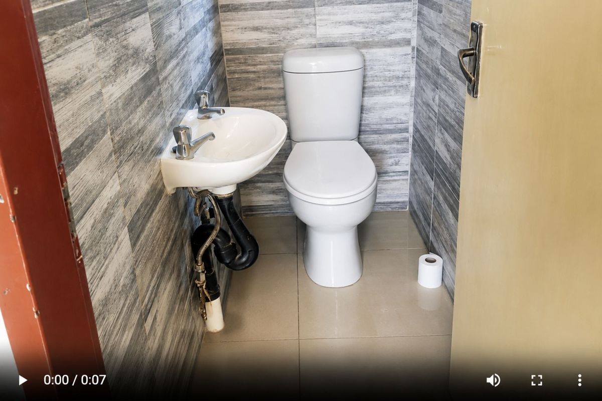 A compact guest bathroom featuring floor-to-ceiling grey wood-look wall tiles, a wall-mounted basin, and a standard toilet.