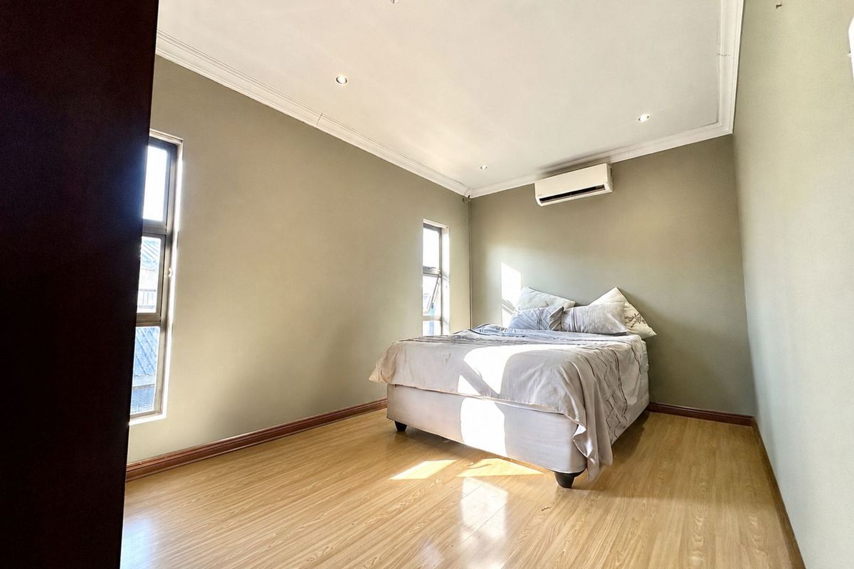 A well-lit bedroom featuring laminate flooring, recessed ceiling lighting, crown molding, and a wall-mounted air conditioning unit.