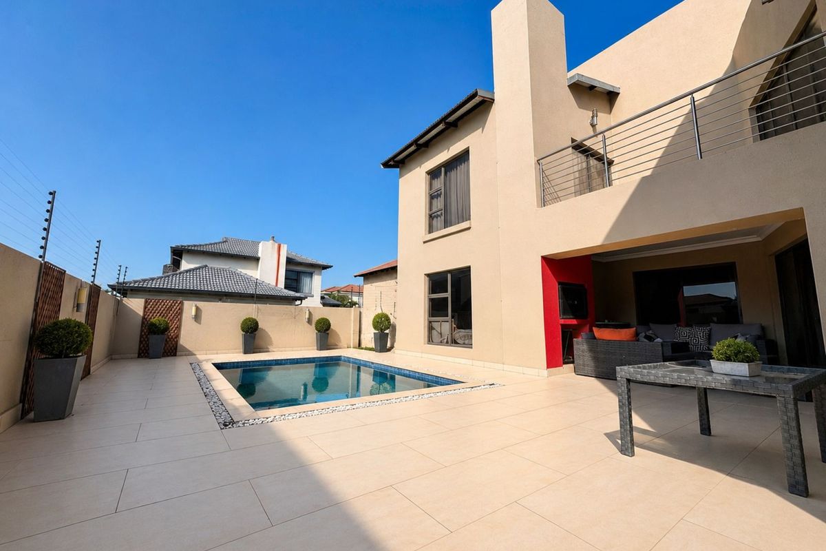 A modern rear exterior featuring a tiled patio, a swimming pool with mosaic tiling, and a covered outdoor entertainment area with a built-in fireplace.