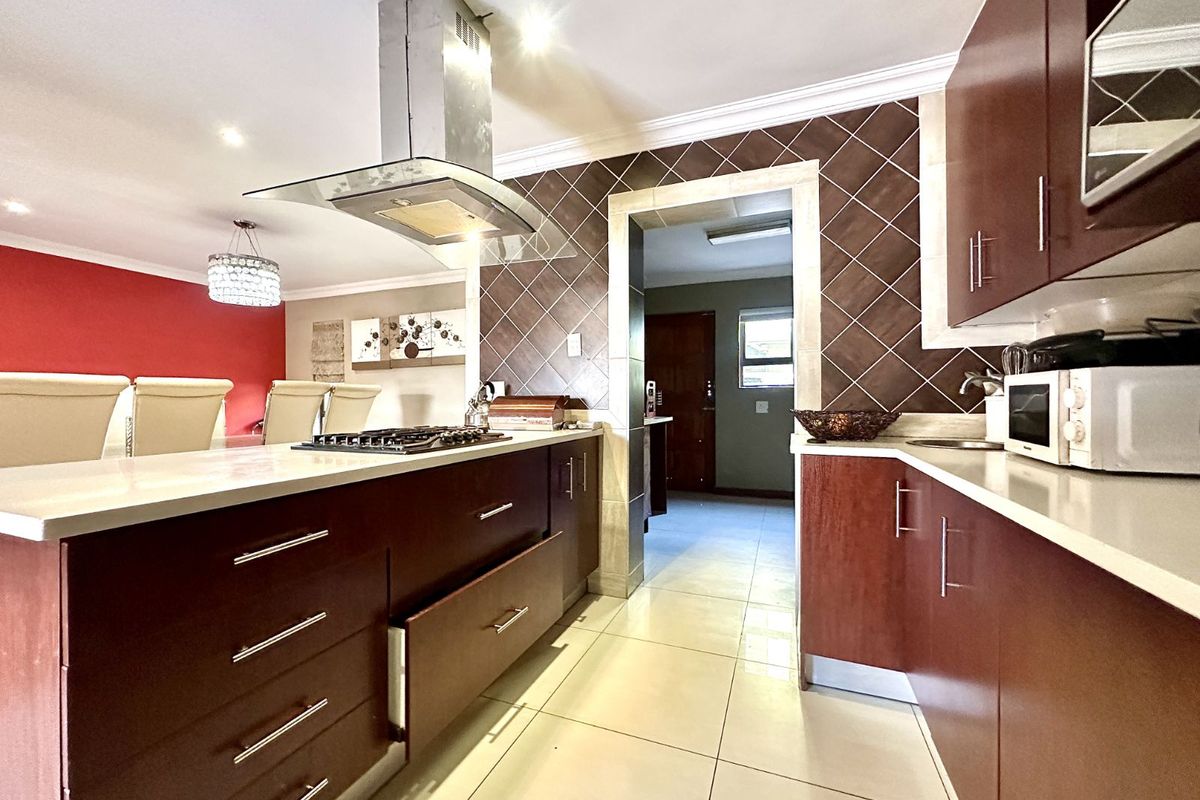 Modern kitchen featuring dark wood cabinetry, stone countertops, a central island with a built-in gas hob, and a stainless steel extractor fan.