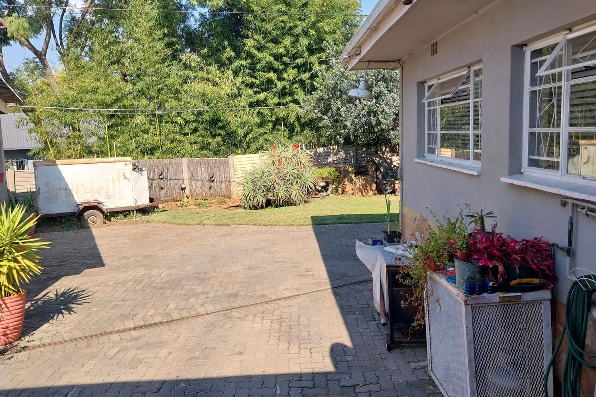 A rear exterior view of the property featuring a paved driveway, garden area, and perimeter fencing.