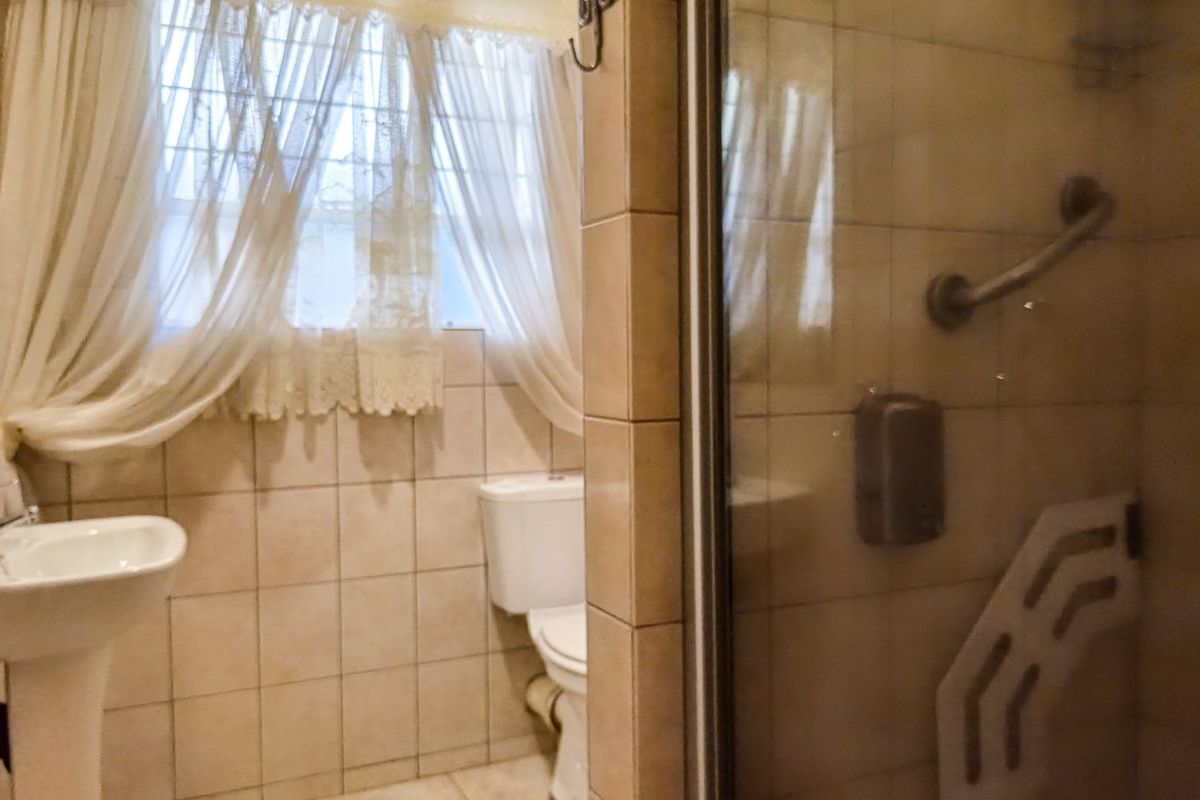 A functional bathroom featuring a pedestal basin, toilet, and a glass-enclosed shower with a grab rail.