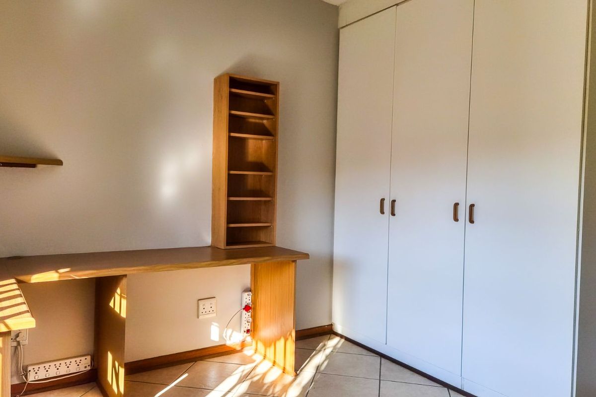 A bedroom featuring built-in white wardrobes and a fixed wooden desk unit with integrated shelving.