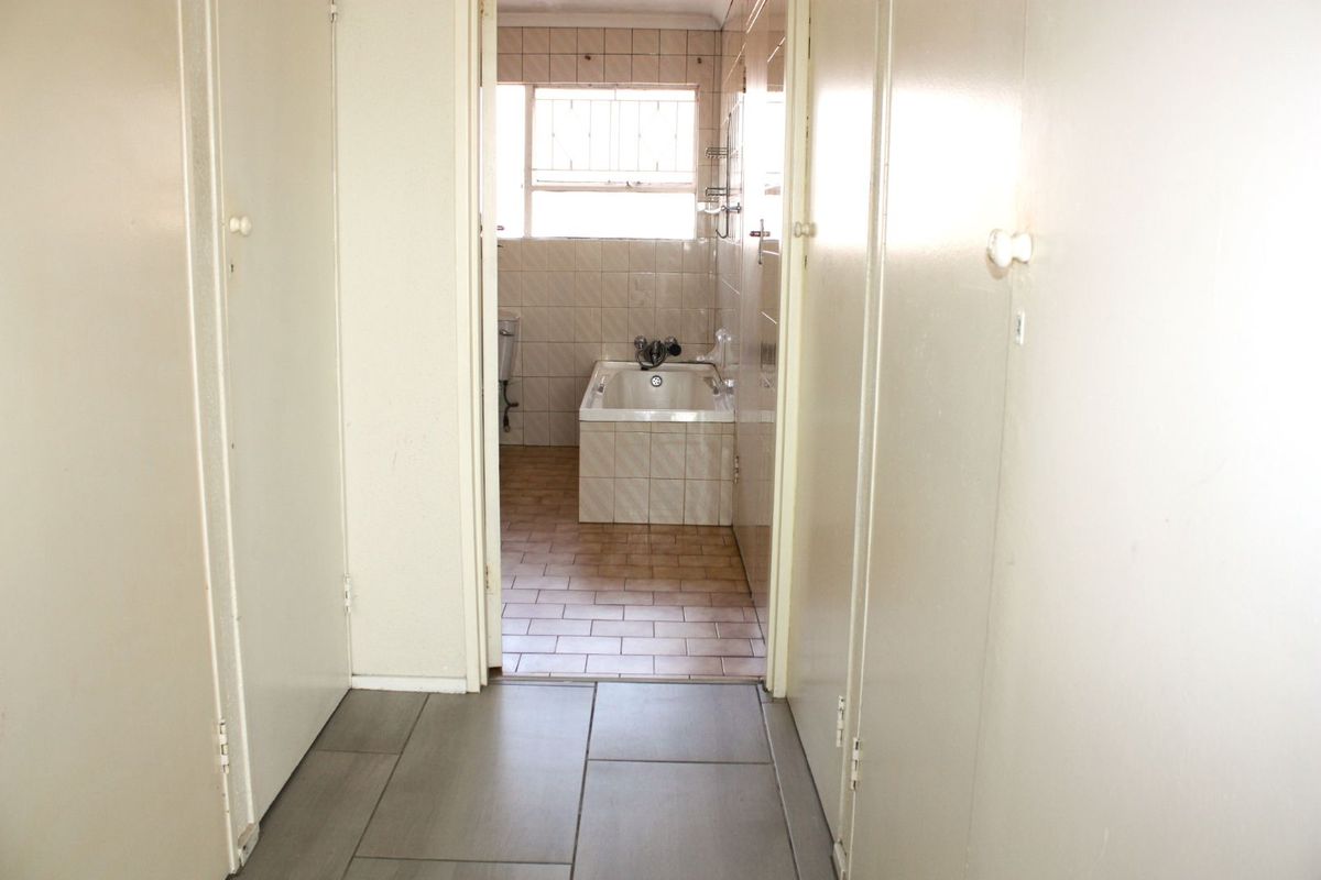 A view from a hallway into a dated bathroom featuring a built-in bathtub, tiled walls, and tiled flooring.