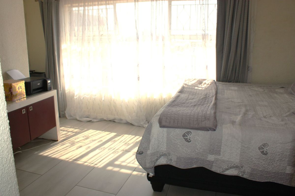 A bedroom featuring tiled flooring and large windows with security bars, allowing for ample natural light.