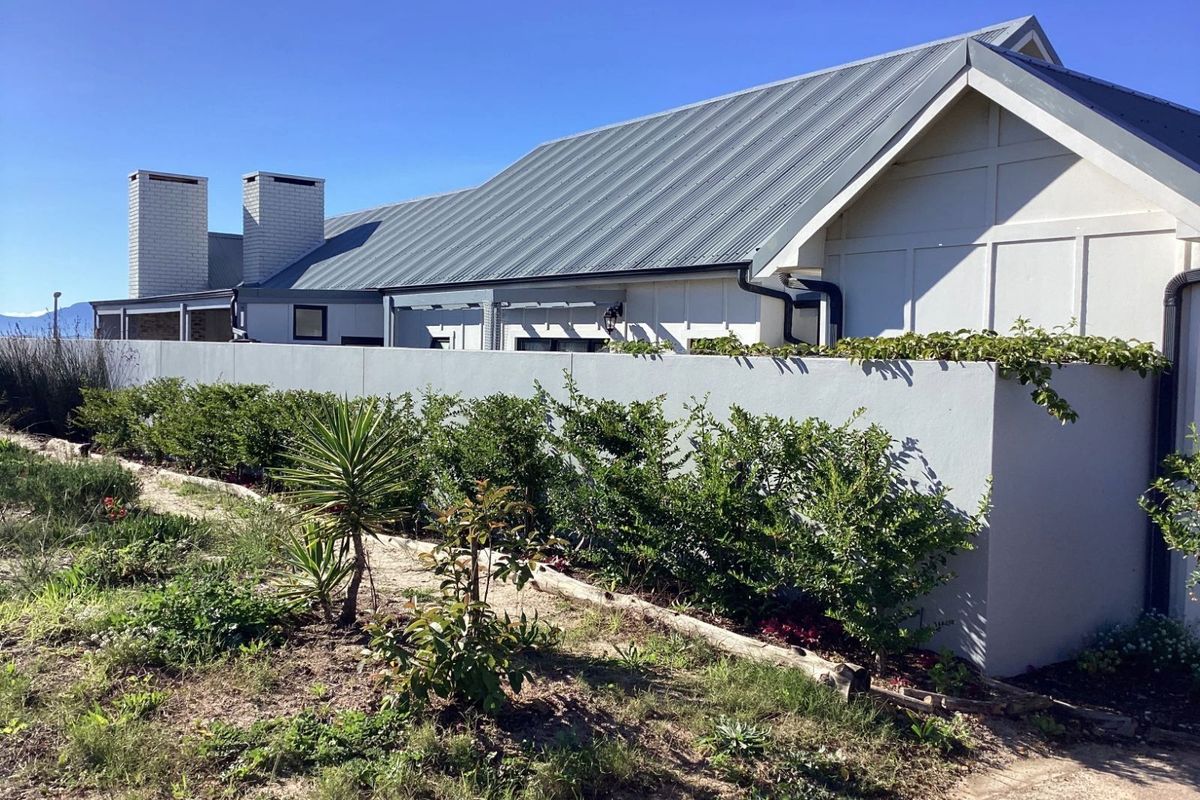 A view of the rear exterior of the house, featuring a metal roof, dual chimneys, and a perimeter wall with landscaped garden beds.
