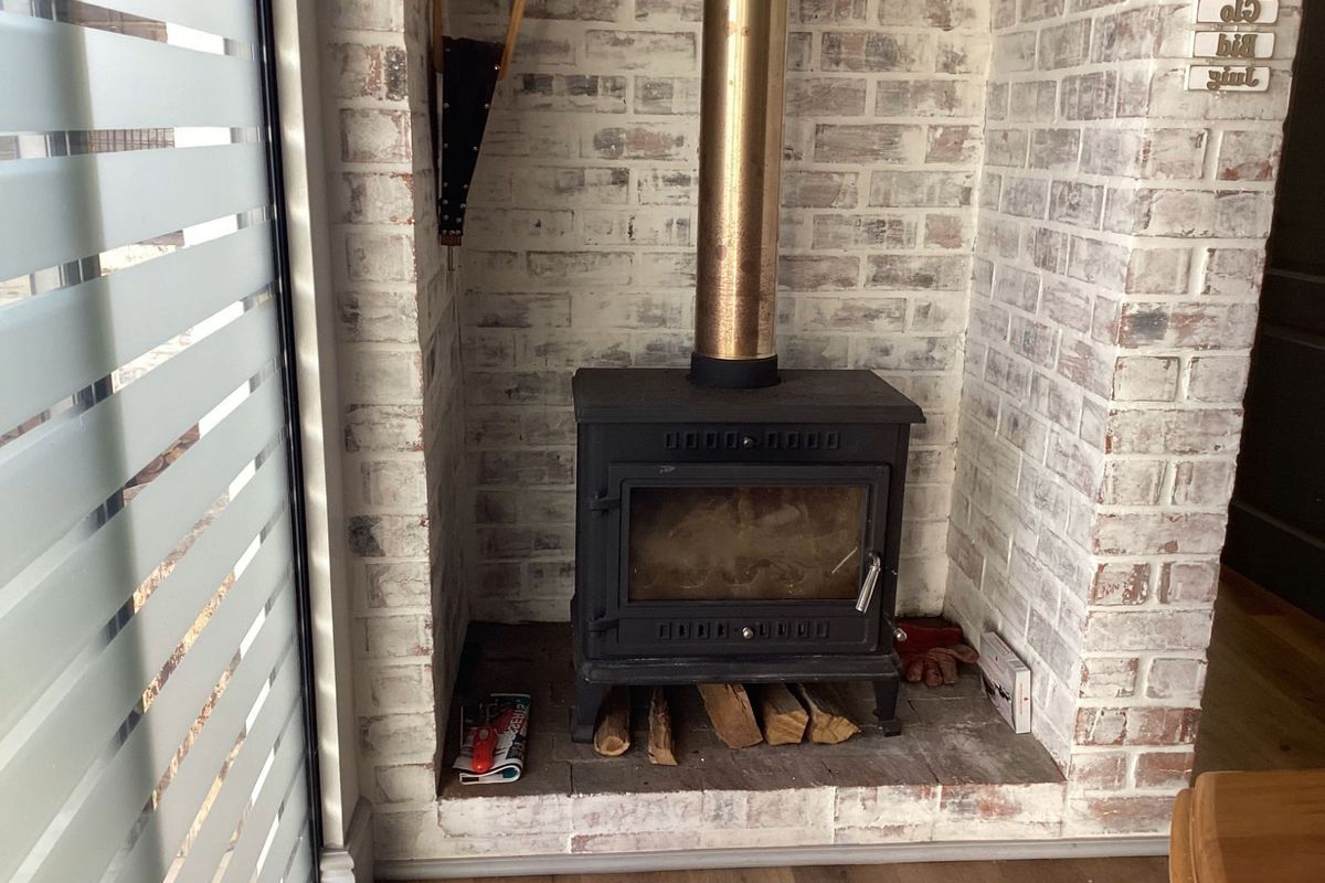 A cozy living area featuring a freestanding wood-burning stove set within a rustic whitewashed brick fireplace surround.