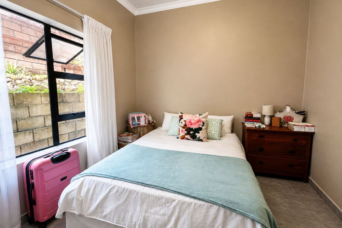 A cozy bedroom featuring tiled flooring, neutral wall tones, and a large window overlooking a retaining wall.