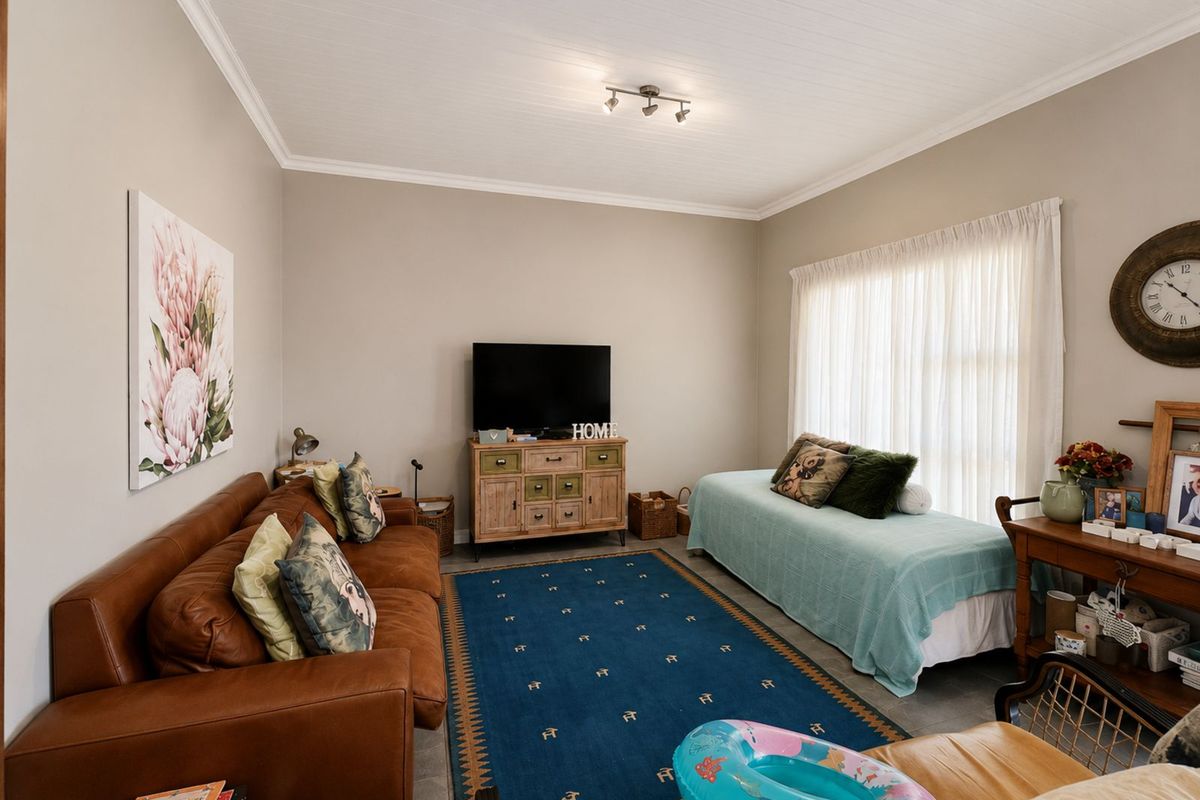 A comfortable living room featuring neutral wall tones, crown molding, tiled flooring, and large windows with sheer curtains allowing natural light.