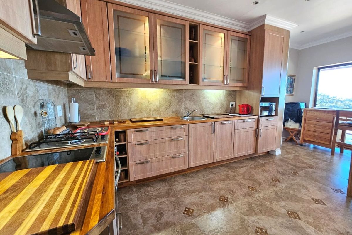 A well-appointed kitchen featuring wood-finish cabinetry, stone-look tiled flooring, a built-in gas hob, extractor fan, and integrated sink with stone backsplash.