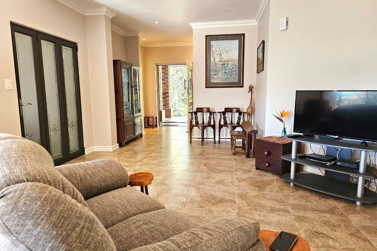 Spacious living area featuring neutral tiled flooring, recessed downlighting, and double glass-panelled doors leading to an outdoor space.