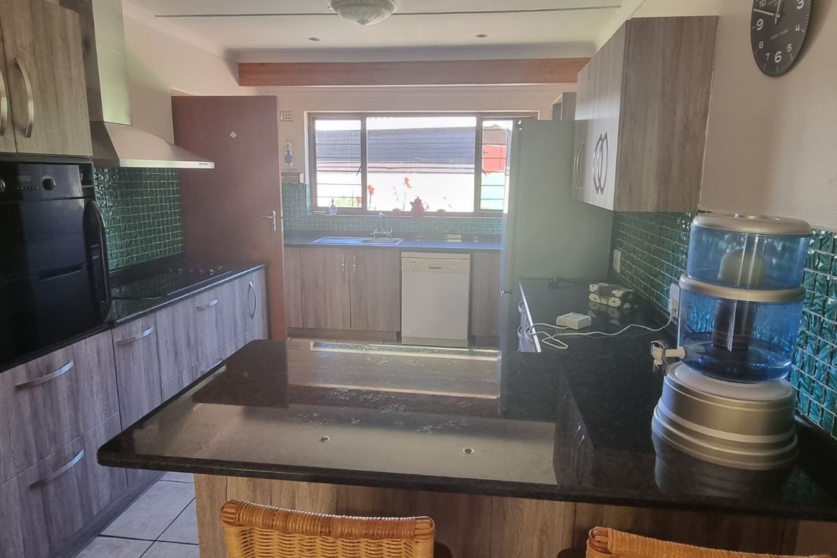 A functional kitchen featuring dark granite countertops, wood-look cabinetry, a built-in oven, and a green tiled splashback with a breakfast bar island.