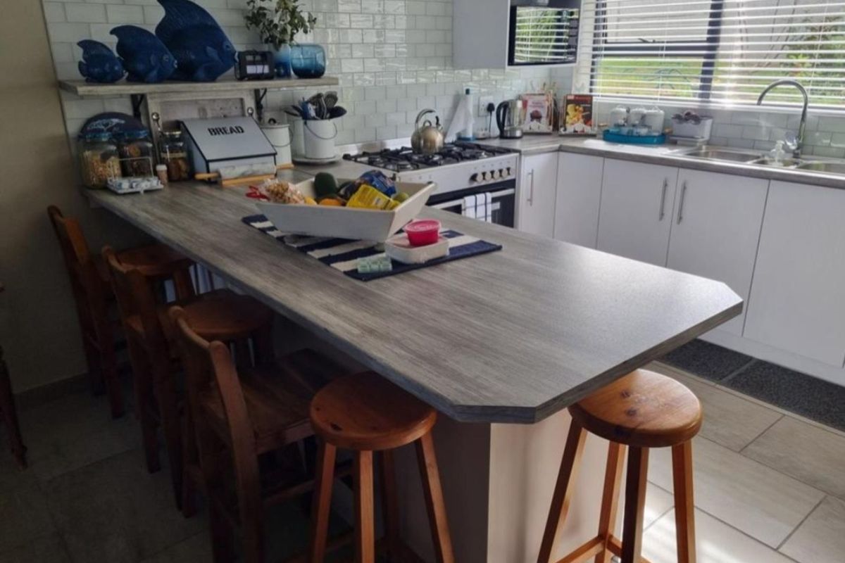 A functional kitchen featuring a breakfast bar, subway tile backsplash, built-in gas hob, oven, and white cabinetry with a stainless steel sink.