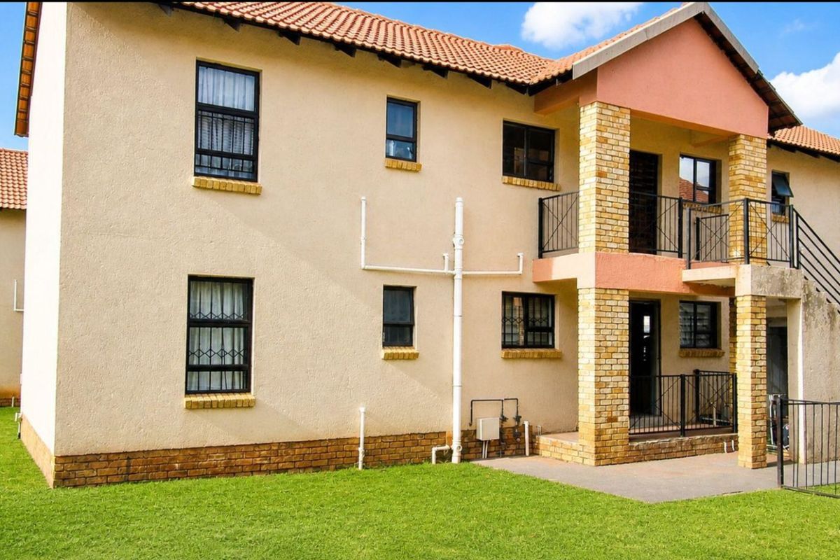 Exterior view of a multi-story apartment building featuring a tiled roof, brick accents, and ground-level access with a small lawn area.