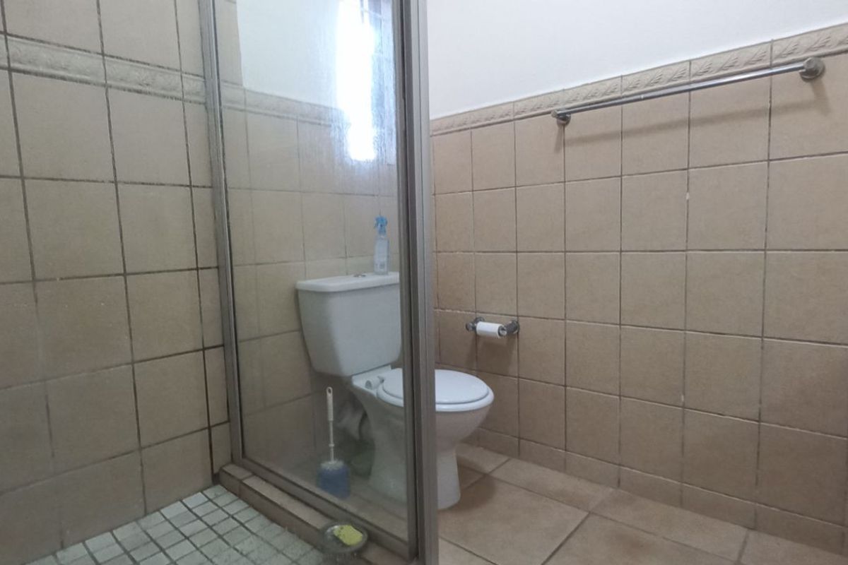 A dated bathroom featuring a glass-enclosed shower, ceramic wall tiles, and standard toilet fixture.