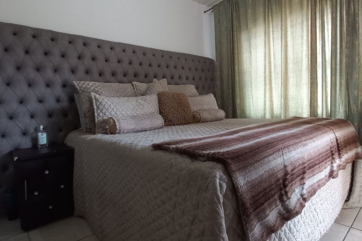 A bedroom featuring a large tufted headboard and tiled flooring, with natural light filtering through window curtains.
