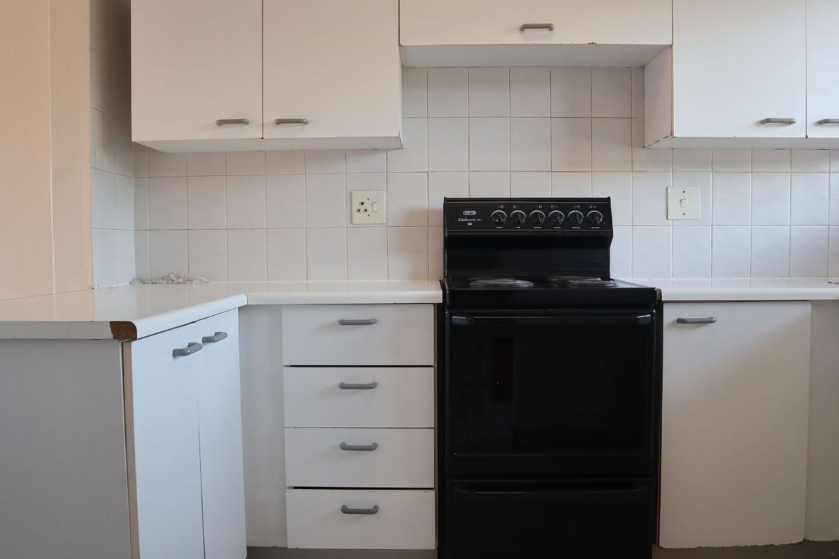 A functional kitchen featuring white cabinetry, tiled splashbacks, and a freestanding black electric stove.