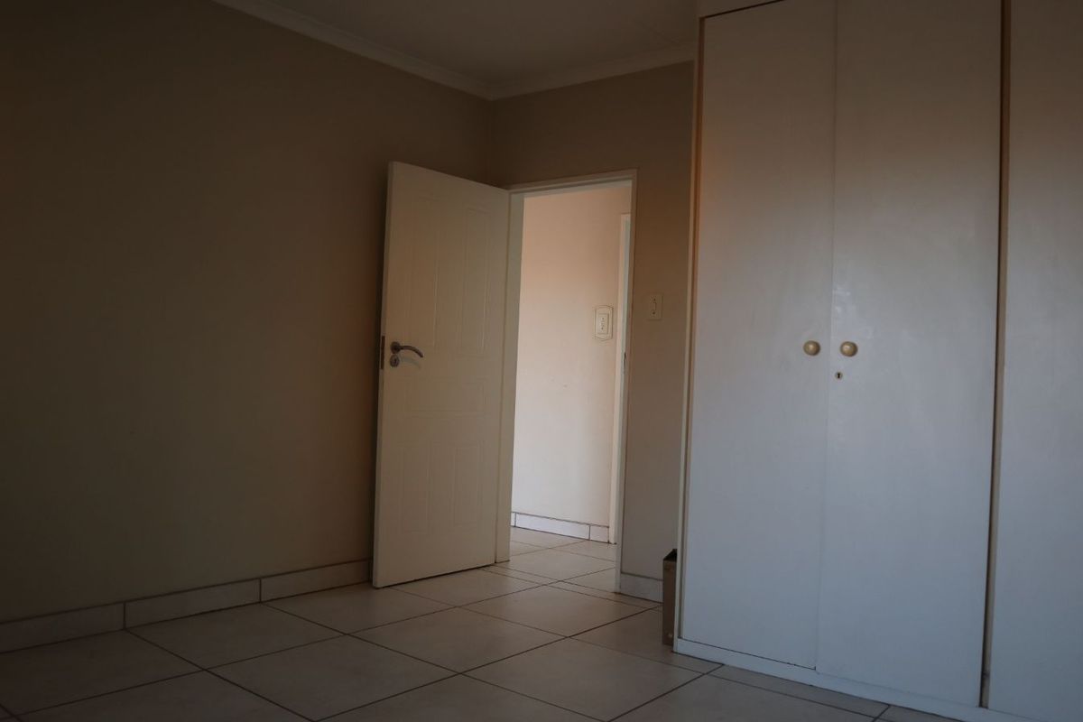 A bedroom featuring tiled flooring and built-in cupboards, with a doorway leading to an adjacent hallway.