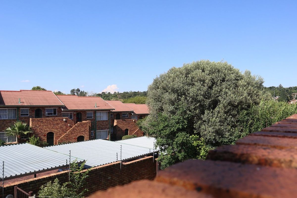 View of the apartment complex exterior featuring face-brick facades, tiled roofing, and surrounding mature trees.