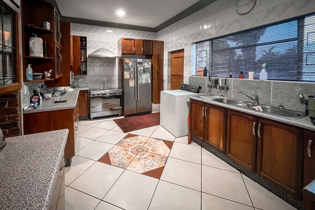 Spacious kitchen featuring wooden cabinetry, tiled flooring with decorative inlay, stainless steel stove, and a double basin sink with large window views.