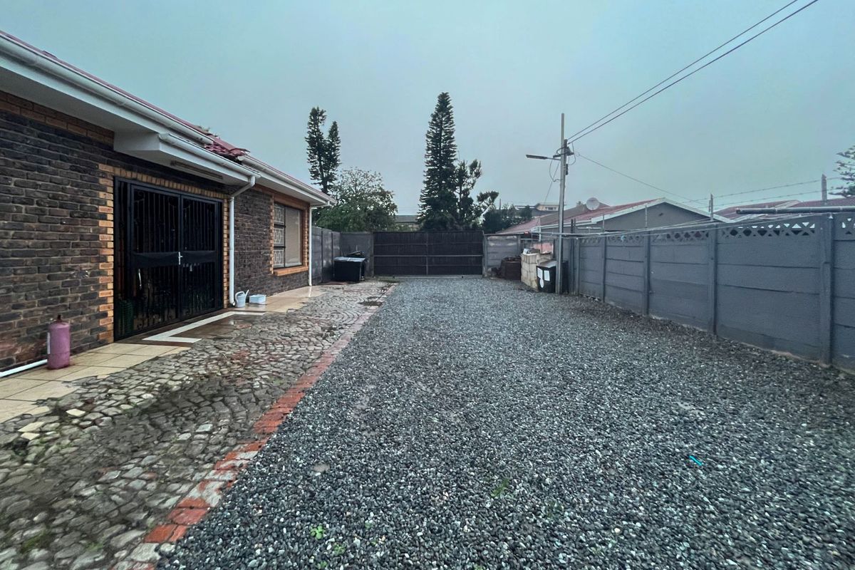 A side exterior view of the property featuring a gravel driveway, paved walkway, and perimeter boundary walls.