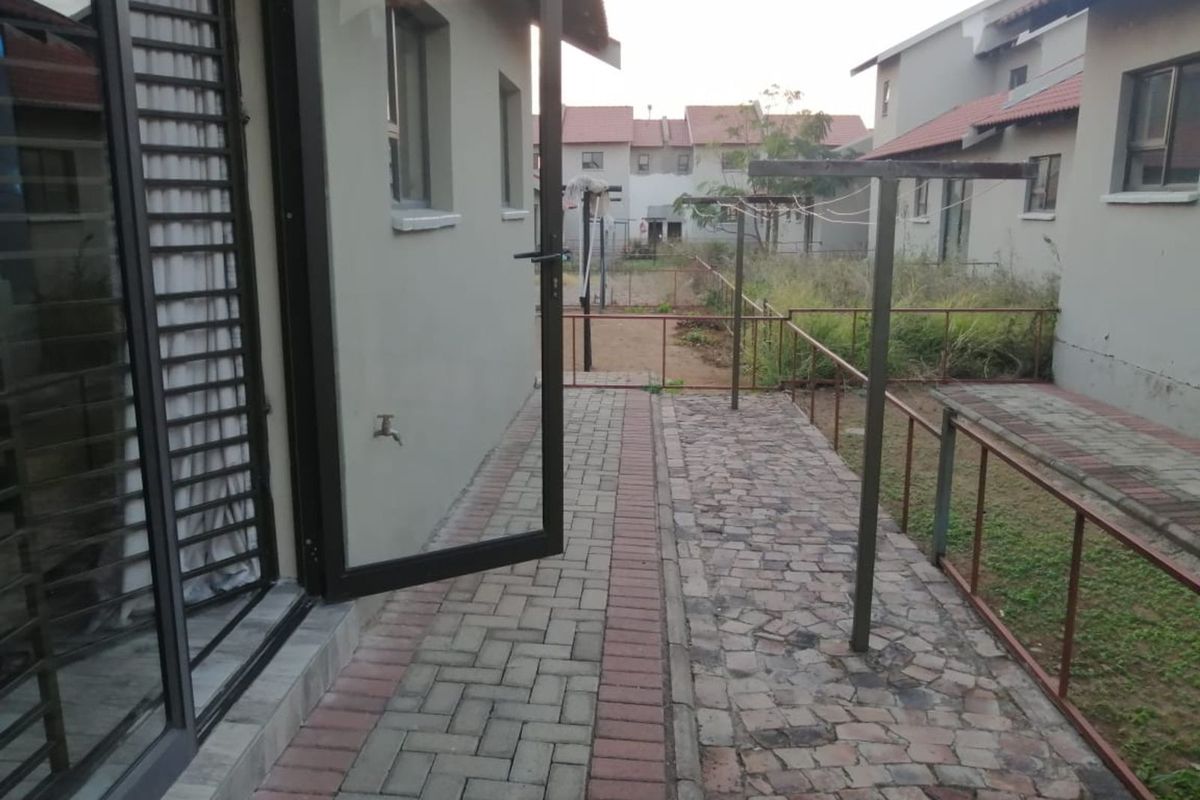 A rear exterior view of the townhouse featuring a paved walkway, metal fencing, and an outdoor drying area leading to a small garden space.