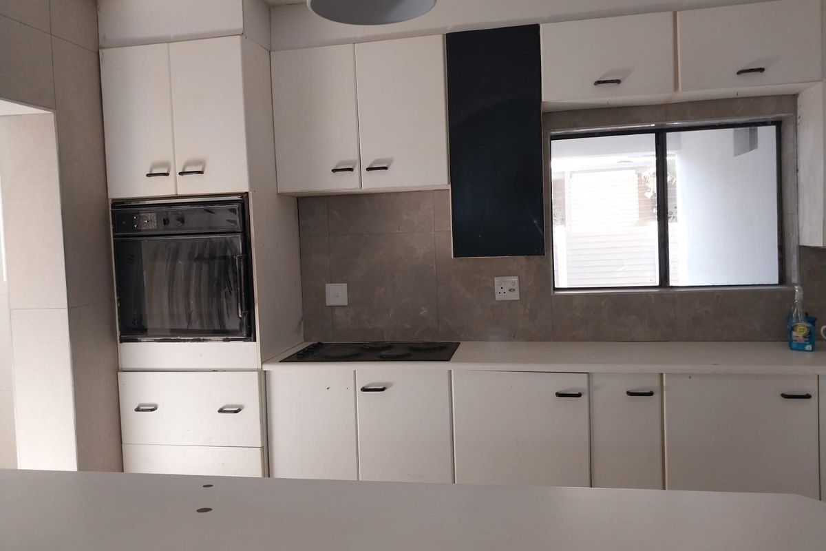 A functional kitchen featuring white cabinetry, a built-in oven, a black hob, and neutral tiled splashbacks with a window for natural light.