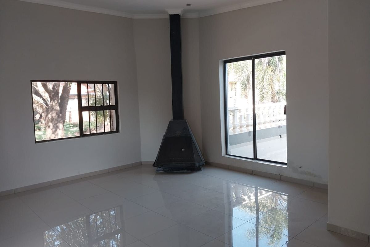 Spacious living area featuring polished tile flooring, a corner-mounted fireplace, and large windows providing natural light and garden views.