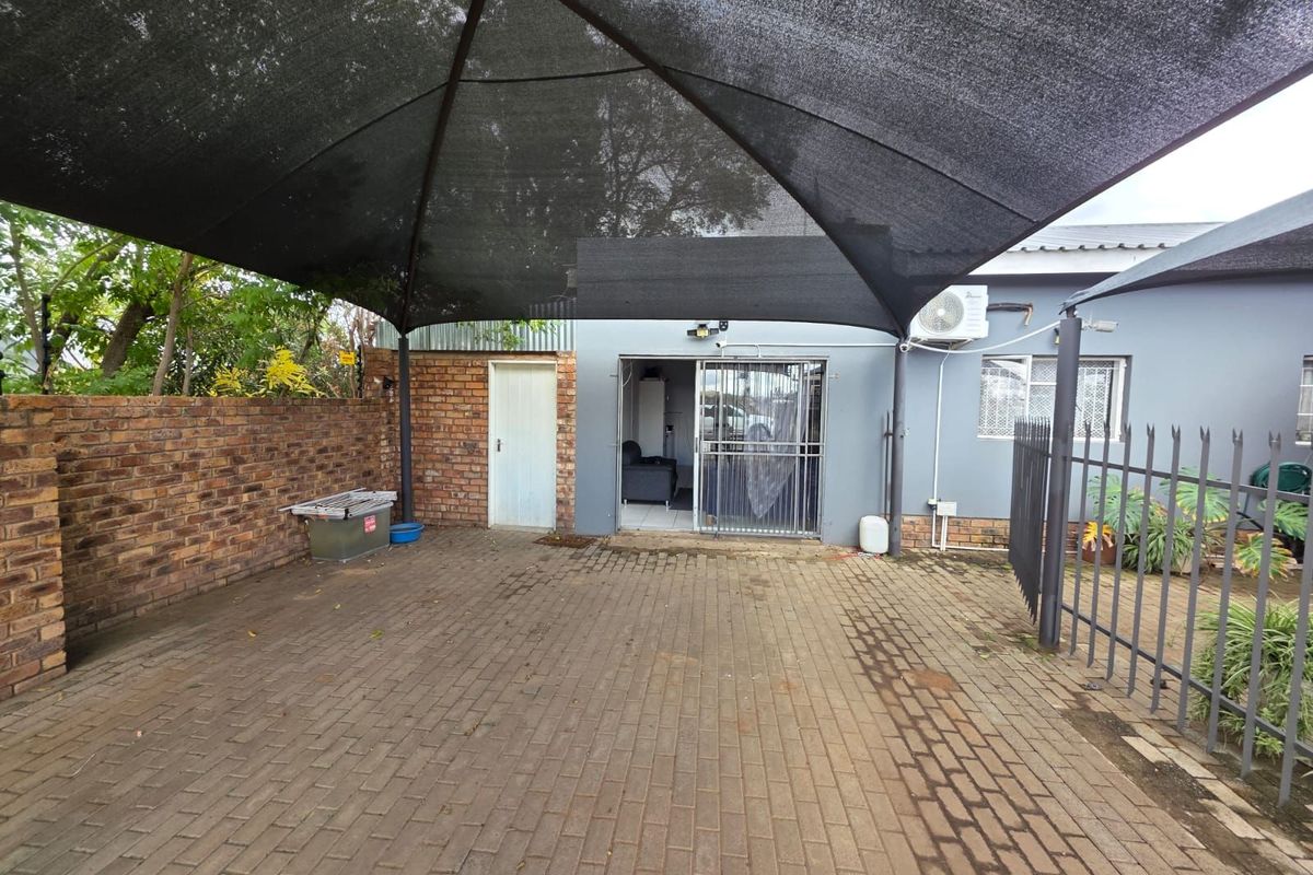 A paved outdoor area featuring a large shade sail, brick boundary wall, and direct access to the main dwelling via a security gate.