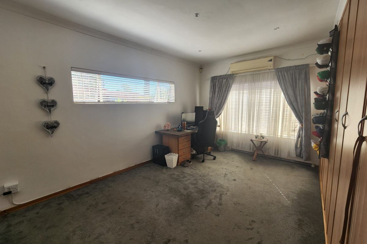 A bedroom featuring built-in wooden wardrobes, carpeted flooring, and a wall-mounted air conditioning unit.