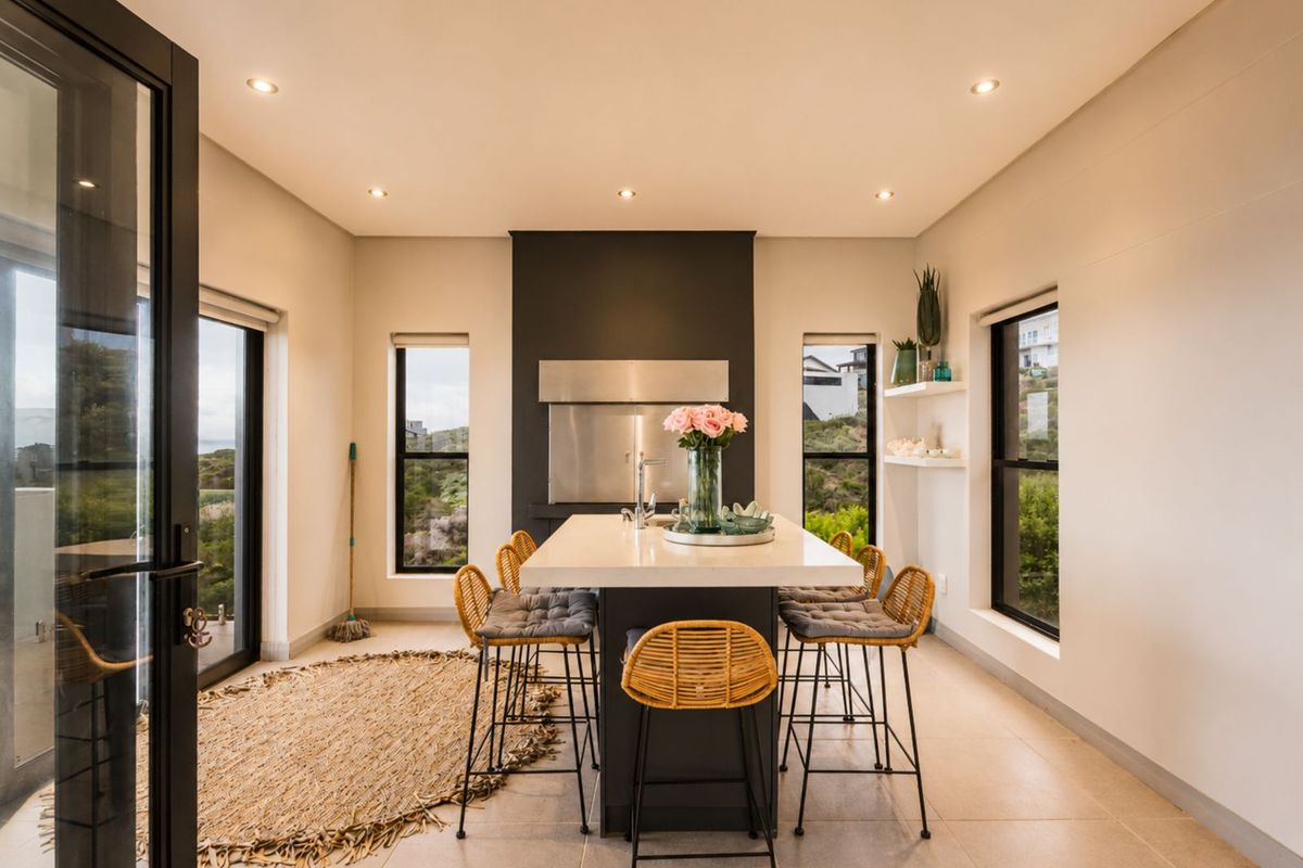 Modern kitchen featuring a central island with integrated sink, sleek cabinetry, and a built-in stainless steel fireplace, complemented by large windows and recessed lighting.