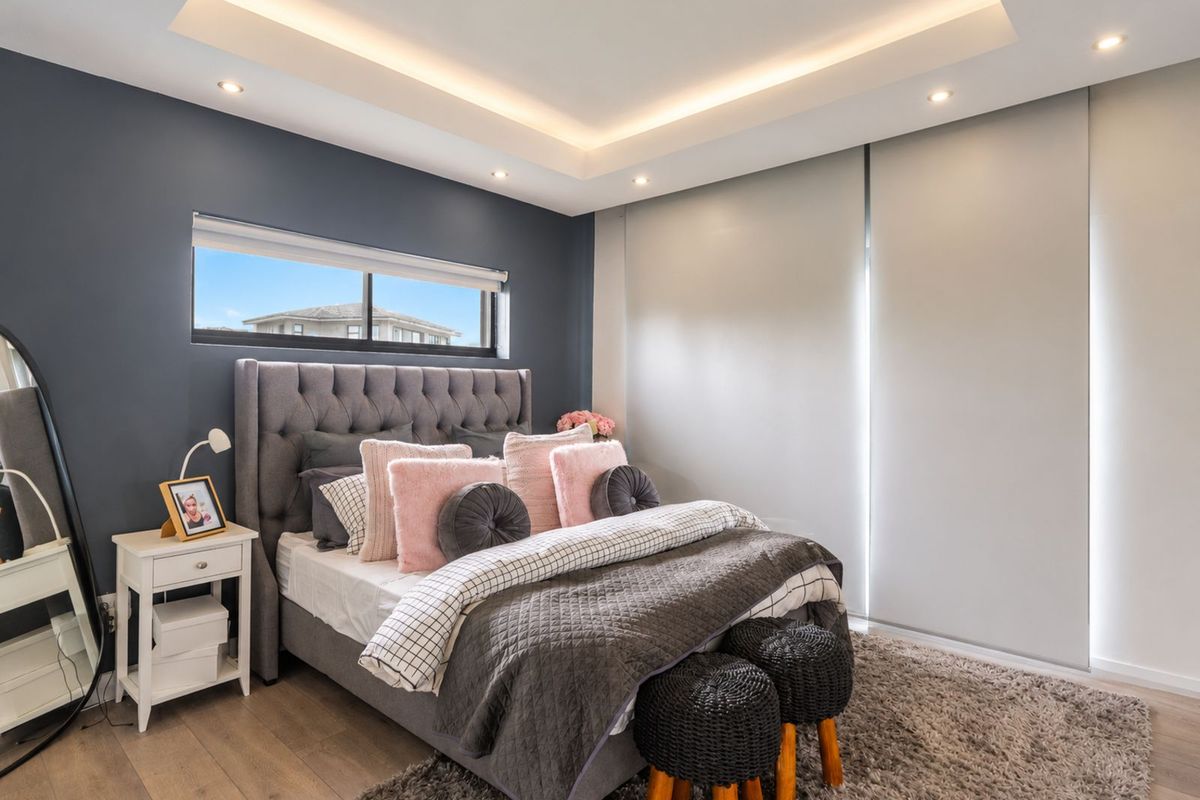 Modern bedroom featuring a recessed tray ceiling with integrated LED lighting, dark feature wall, and large built-in wardrobe with sliding doors.