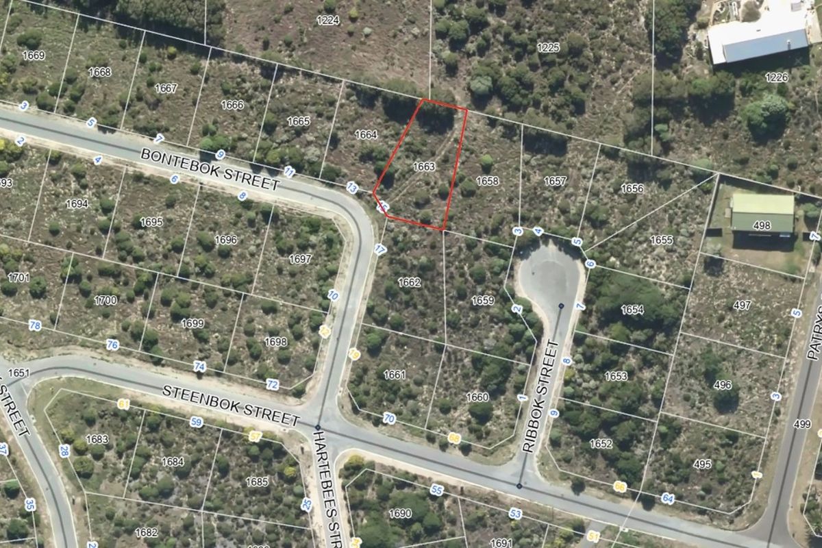 Aerial view of a vacant residential plot highlighted in red, situated within a developed street network with surrounding natural vegetation.