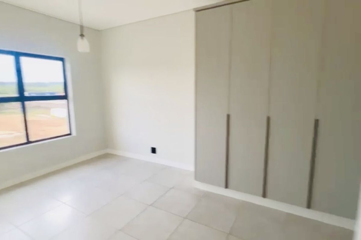 A bright, modern bedroom featuring neutral tiled flooring, built-in cabinetry, and a large window providing natural light.